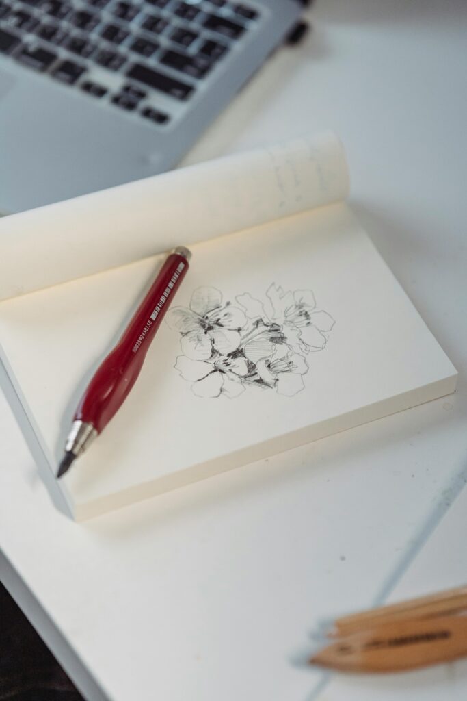 Close-up of a floral sketch on a notepad with a red pen on a desk.